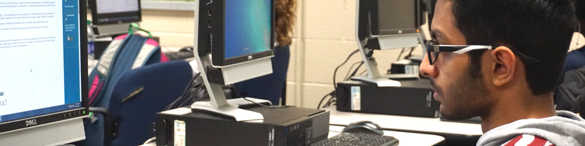Student in glasses and striped hoodie staring at computer monitor Student in glasses and striped hoodie staring at computer monitor