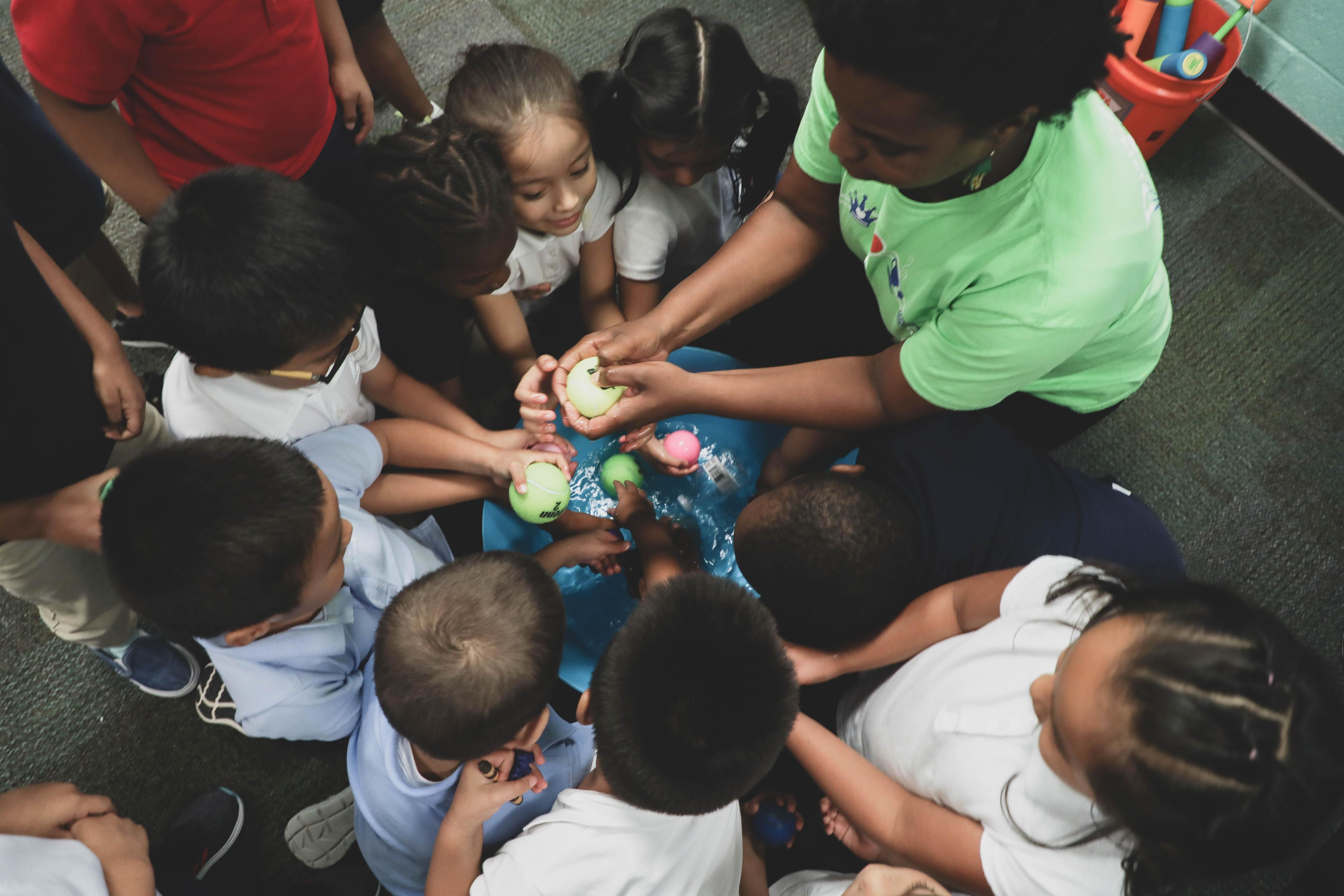 Students gathered around a bucket filled with water and various balls Students gathered around a bucket filled with water and various balls
