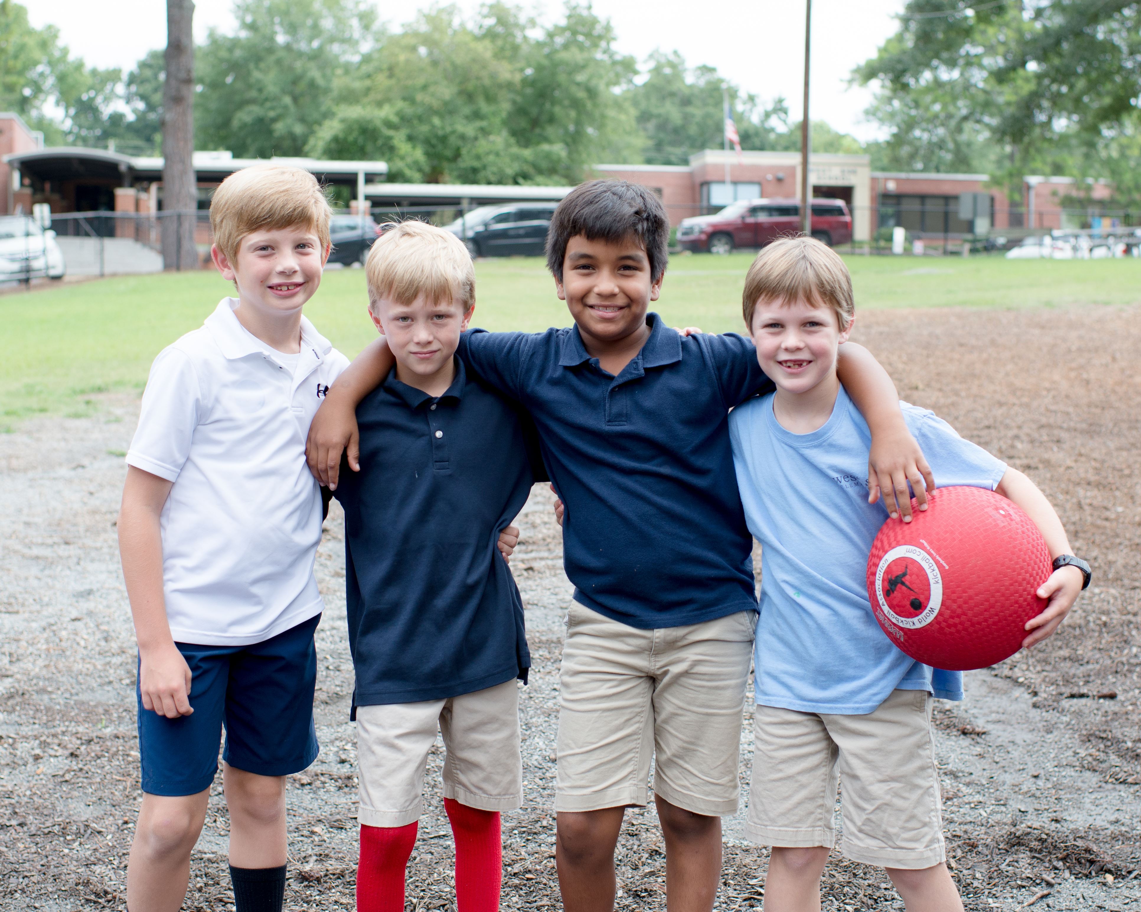 Four students posing together on playground and smiling, one holding red ball Four students posing together on playground and smiling, one holding red ball