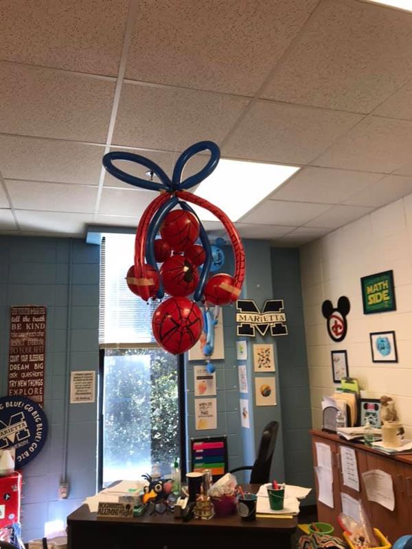 Spider-Man themed balloon bundle floating above teacher desk in classroom