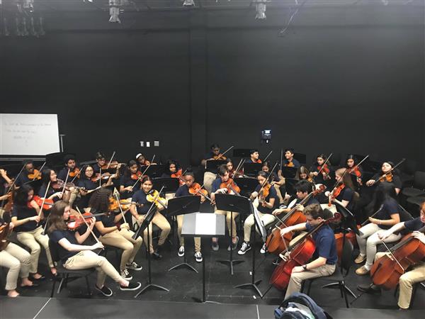 Wide shot of orchestra students rehearsing with various string instruments