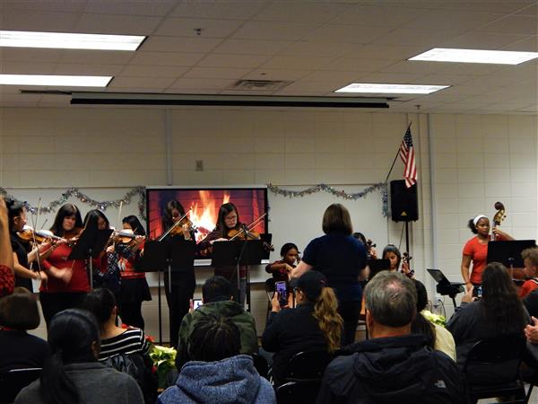 Wide shot of orchestra students and teachers performing in front of classroom of adults