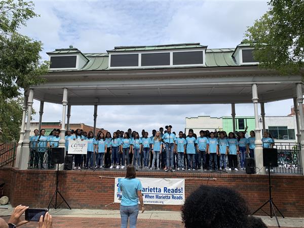 Wide shot of students in blue shirts singing from Marietta Square pavilion
