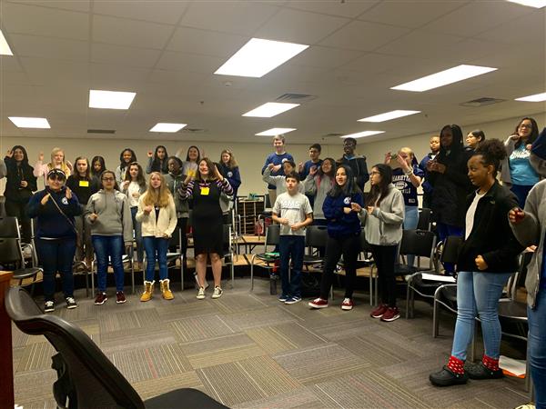 Group of students circled around on chairs and risers in classroom