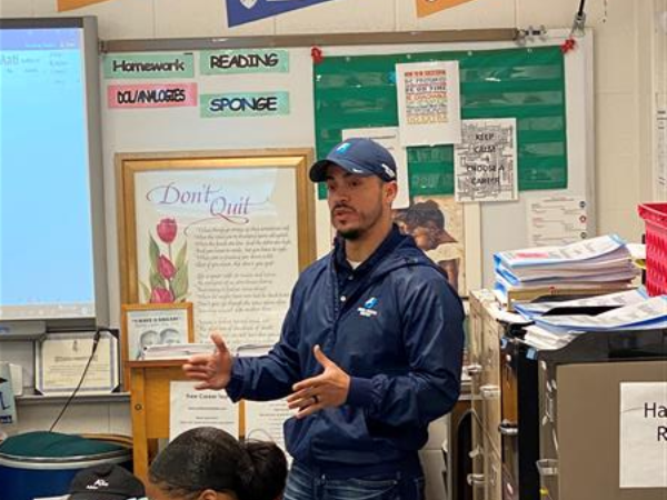 Man in blue hat and jacket addressing students in classroom