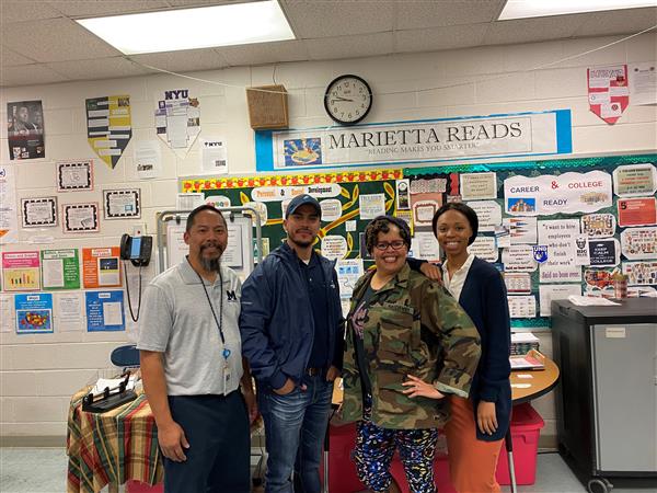 Four adults posing together and smiling in classroom