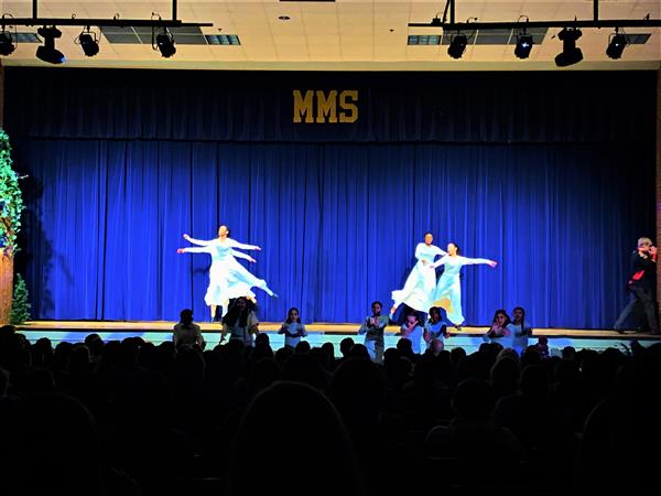 Four students dancing on stage in long blue dresses