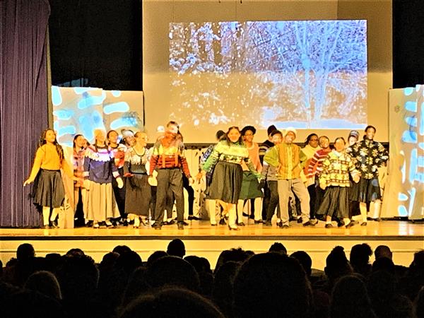 Ensemble student cast on stage during play wearing winter themed sweaters and dancing