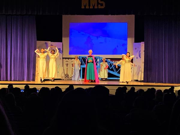 Dance students on stage in yellow dresses and colorful dress