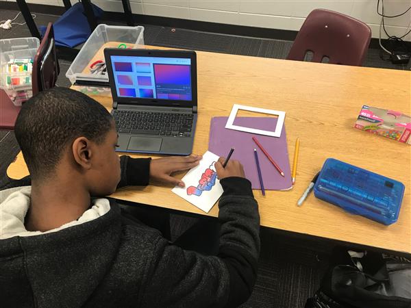 Student with open computer coloring design on paper