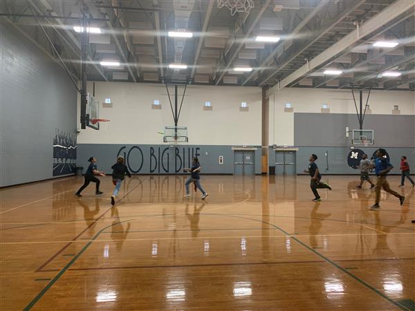 Students playing game of basketball in gymnasium