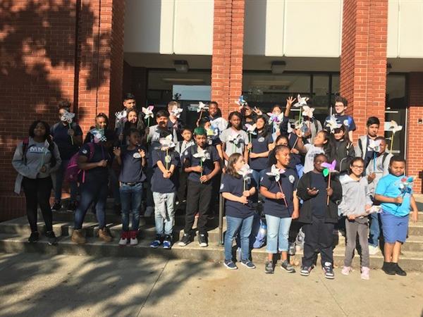 Large group of students holding pinwheels and posing together in front of school