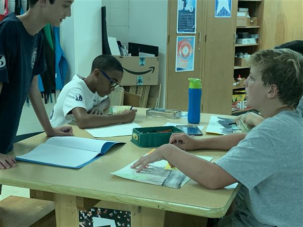 Students conversing while working on art projects at table in classroom