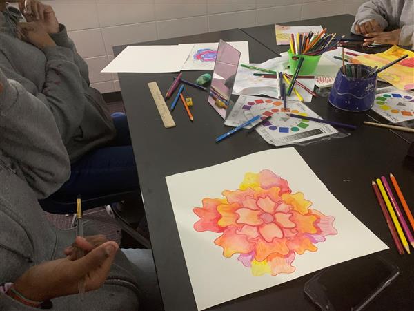 Close-up of student coloring abstract orange flower with colored pencils