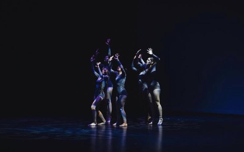 A small group of dancers perform on stage with dark, textured spots of light on them