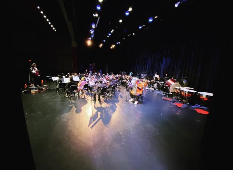 Band students play on stage in the middle of a performance, some students are dressed in a Halloween costume