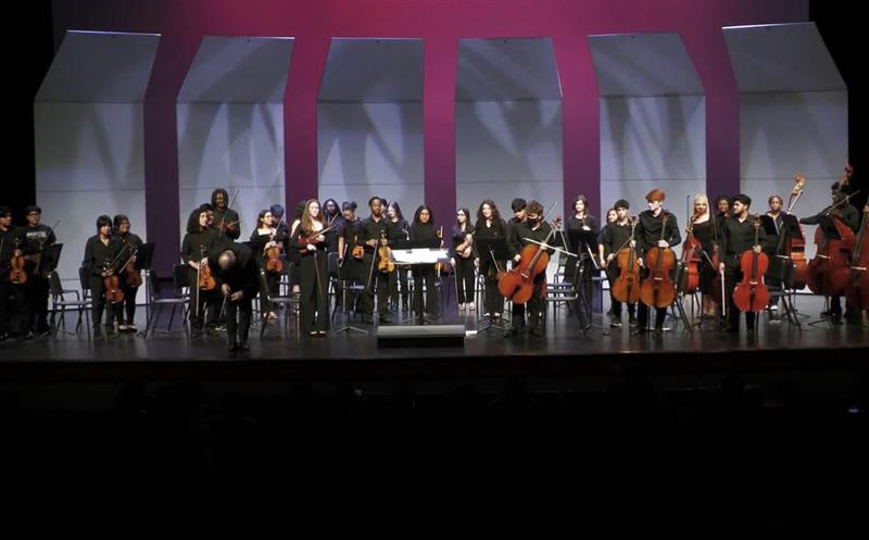 Orchestra students stand on stage with their instruments after a performance