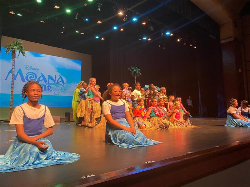 Student cast from Moana Jr performs on stage in costume