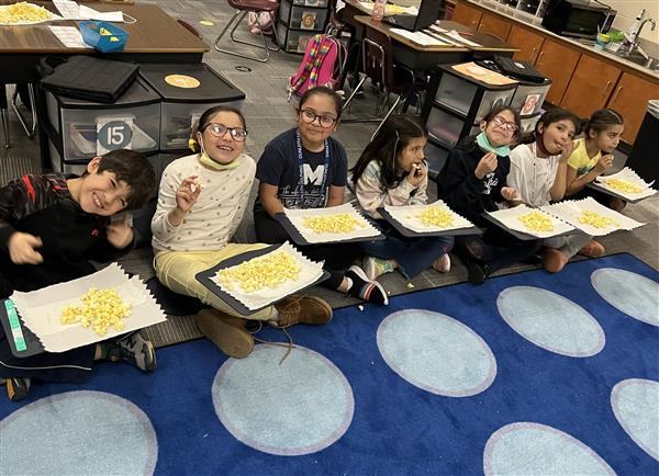 Students sit on the floor with trays of popcorn in their laps