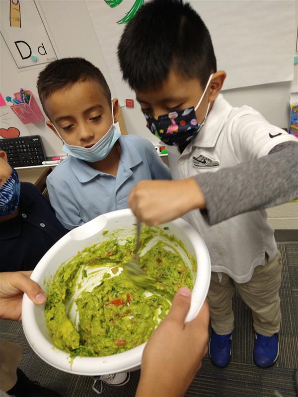 A student mixes up a bowl of guacamole while a peer looks on