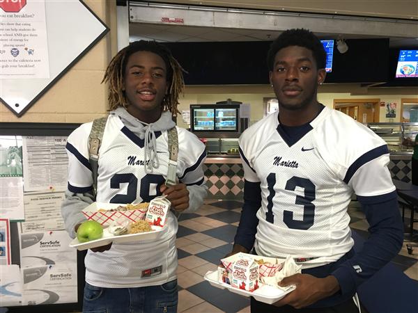 Two Marietta football players in jerseys holding school lunch trays