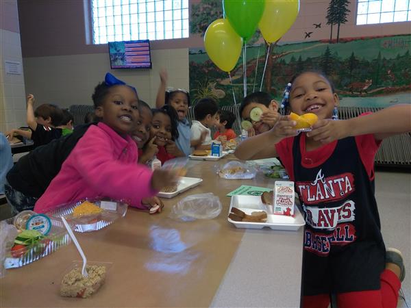 Students at a lunch table smile and display their fresh food