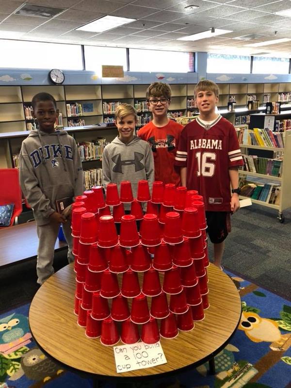 Students standing proudly around round tower made of 100 red plastic cups