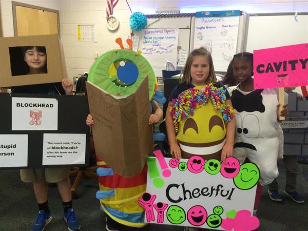 Students dressed in costumes representing words, explained by signs reading Blockhead, Bookworm, Cheerful, and Cavity