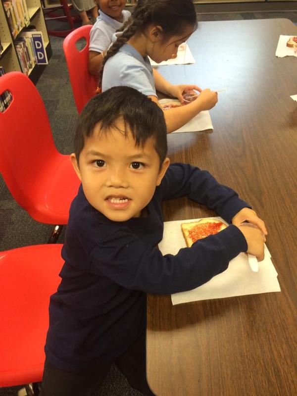 Student seated and smiling while learning the skill of spreading jelly on bread