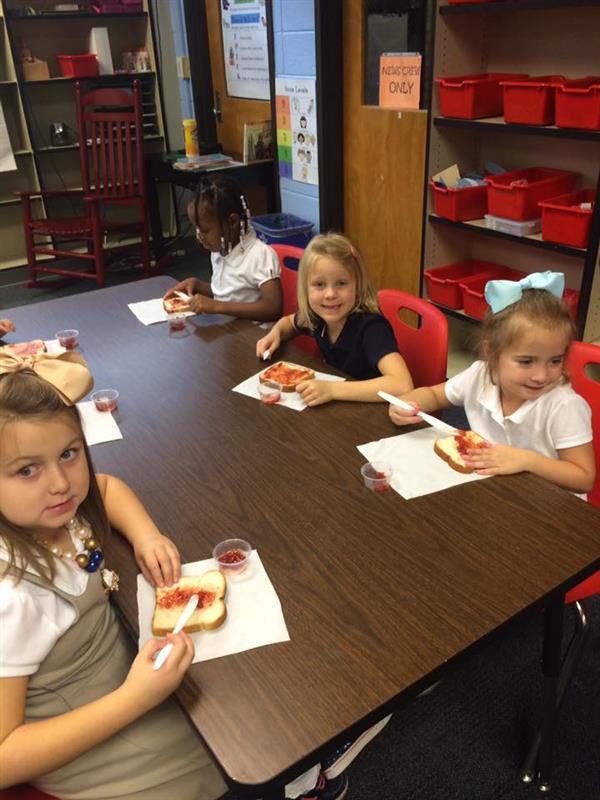 Table of students seated at table spread jelly onto slices of bread